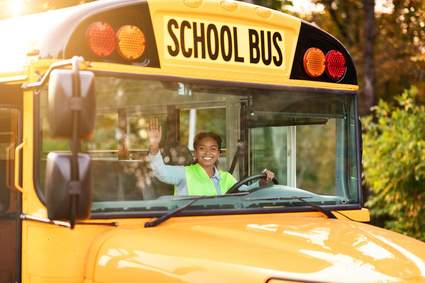 Portrait of joyful young black female driver steering yellow school bus