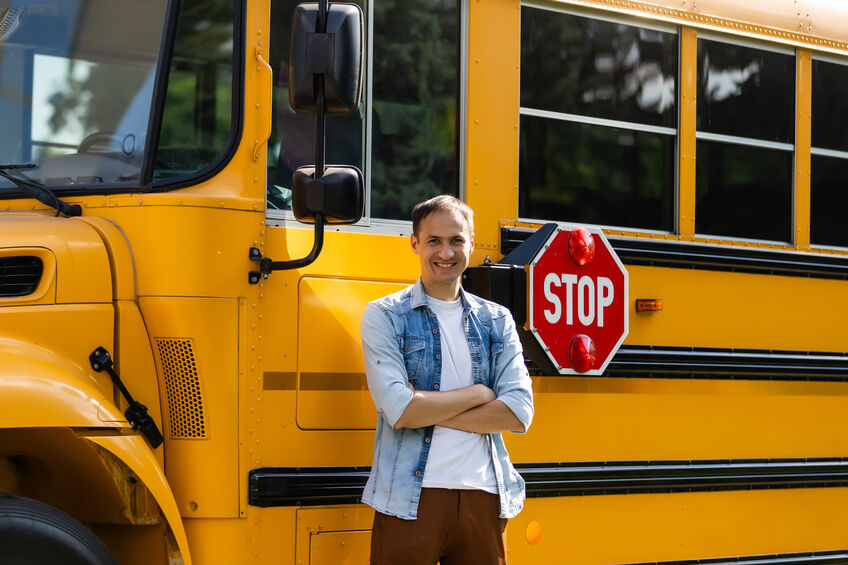 Smiling bus driver looking at camera ready to pick up kids from summer school
