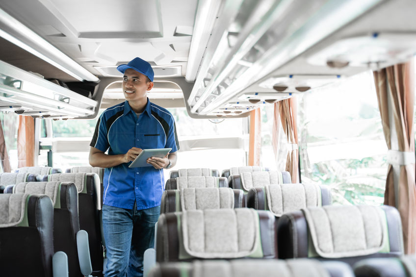 a male bus manager uses a digital tablet while checking shelves inside the bus