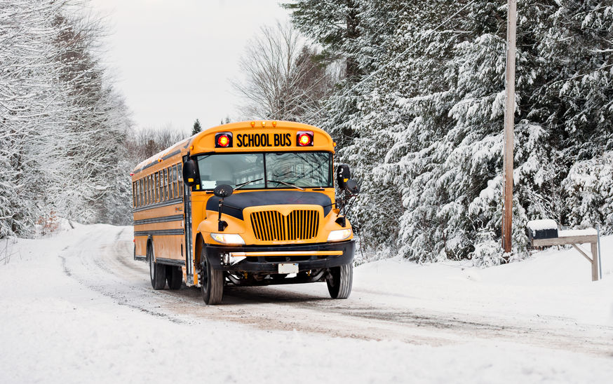 A school bus drives down a snow covered rural country road lined with snow covered trees after a snow storm during the winter season. Series 3 of 3